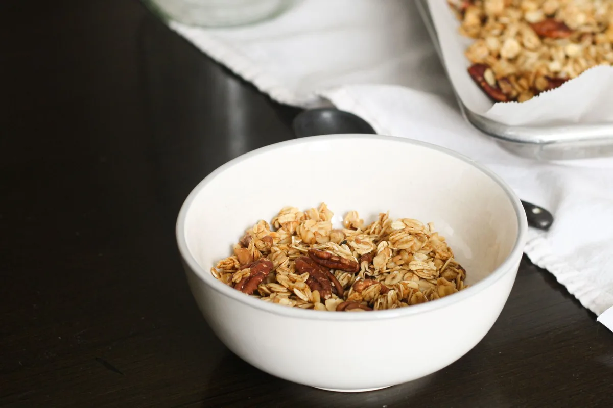 Préparation maison de granola avec flocons d'avoine, fruits secs et miel dans un bol en verre