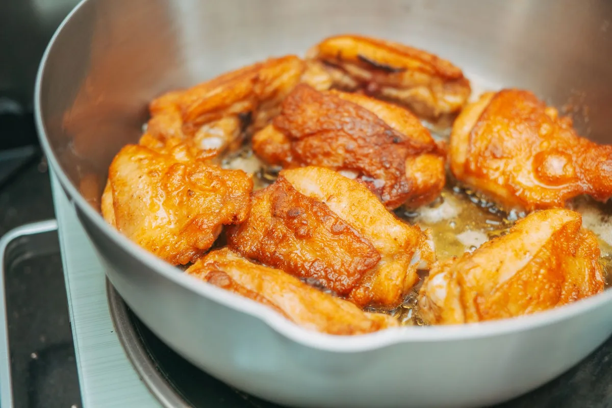Morceaux de poulet dorés et caramélisés dans une poêle avec de l'huile d'olive