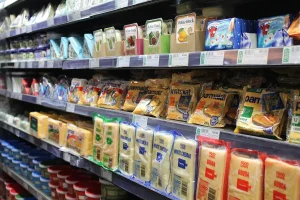 Main d'une personne tenant un emballage de fromage bleu au-dessus d'un réfrigérateur ouvert