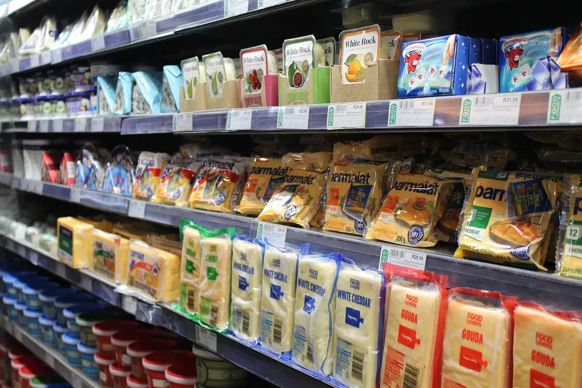 Main d'une personne tenant un emballage de fromage bleu au-dessus d'un réfrigérateur ouvert