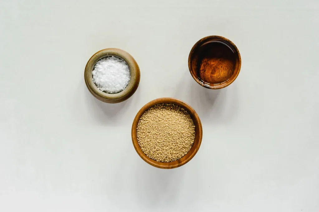 Trois variétés de sel dans des bols : sel fin blanc, gros sel de mer et sel rose, disposés sur une surface en bois de cu