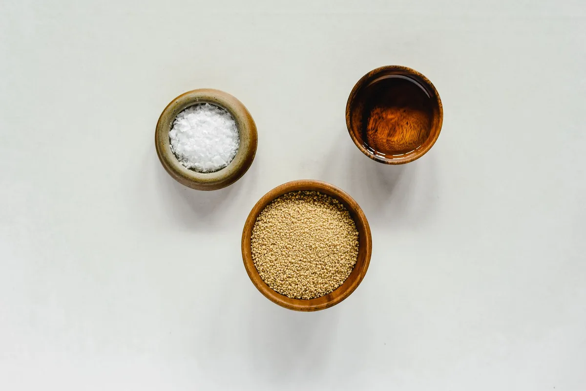 Trois variétés de sel dans des bols : sel fin blanc, gros sel de mer et sel rose, disposés sur une surface en bois de cu