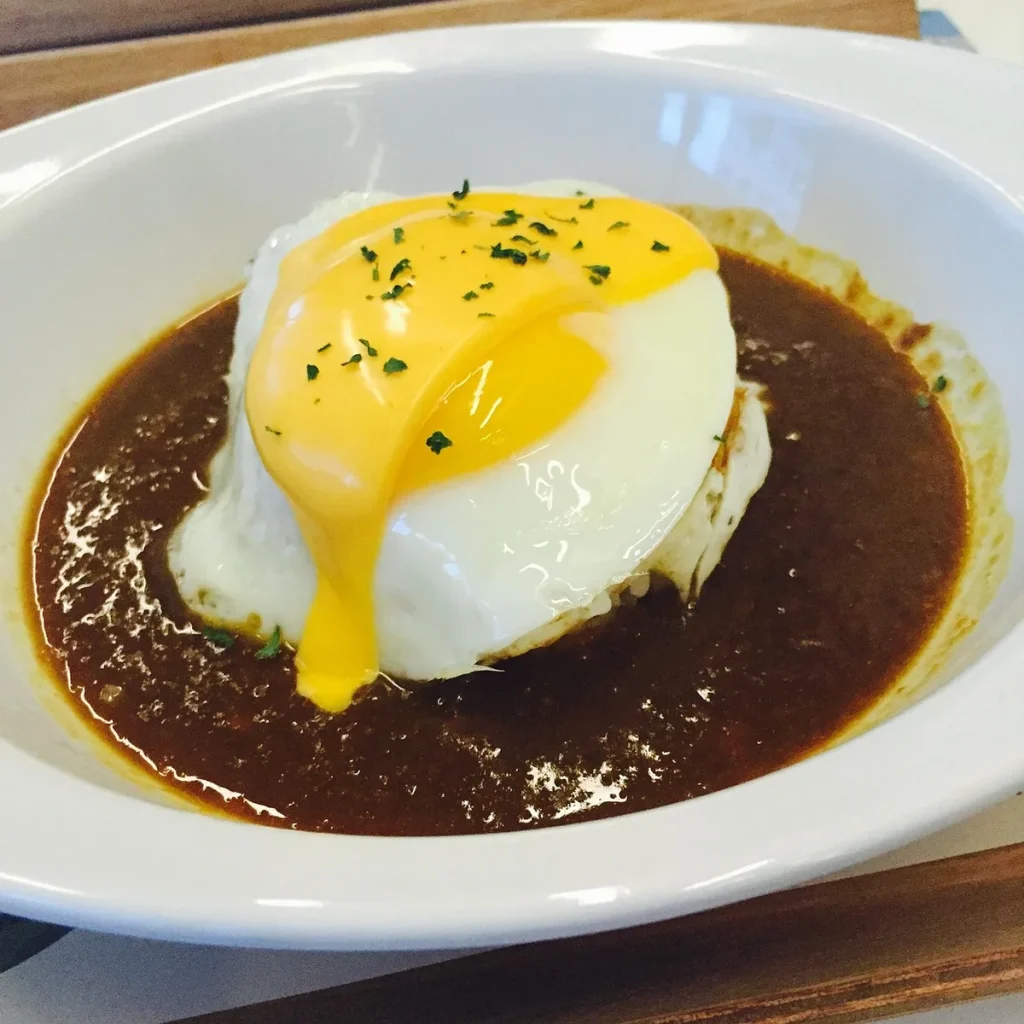 Mains versant une sauce curry crémeuse dorée dans une casserole, entourée d'épices et herbes fraîches