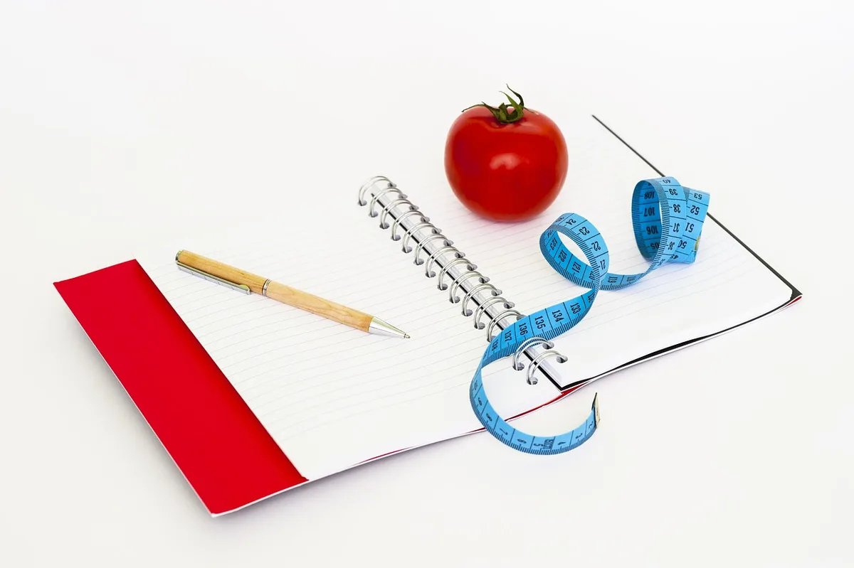 Carnet de menu hebdomadaire posé à côté de courses et d'un calendrier