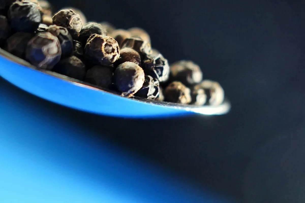 Grains de poivre noir et blanc mélangés sur une planche de cuisine