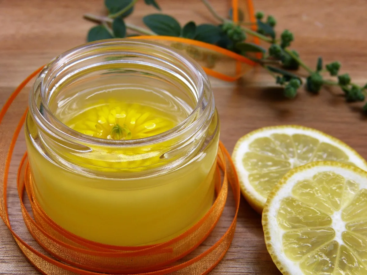 Mains appliquant une crème bio depuis un pot en verre près d'une fenêtre en journée